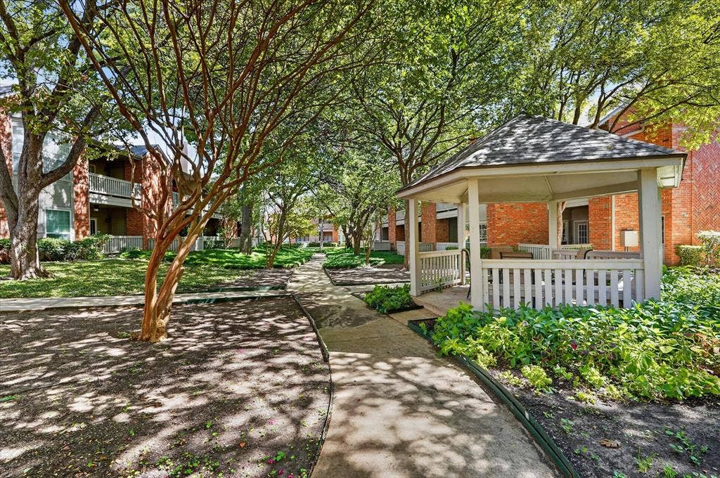 12660 Hillcrest Road, #5204, Dallas, TX 75230 Manicured common grounds featuring mature trees, paved walking paths, a dedicated gazebo, and brick-exterior buildings