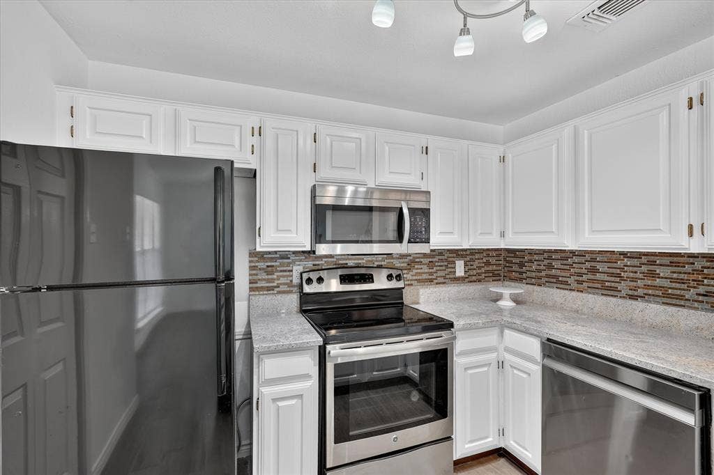 12660 Hillcrest Road, #5204, Dallas, TX 75230 White cabinetry with panel detailing, mosaic tile backsplash, light-toned countertops, stainless steel appliances, and track lighting
