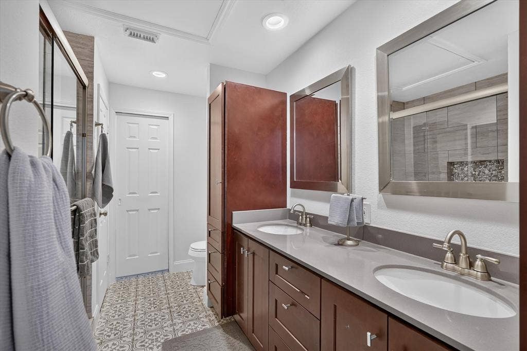 12660 Hillcrest Road, #5204, Dallas, TX 75230 Dual sinks set in a gray countertop, dark wood-finish cabinetry, patterned floor tiling, and rectangular framed mirrors