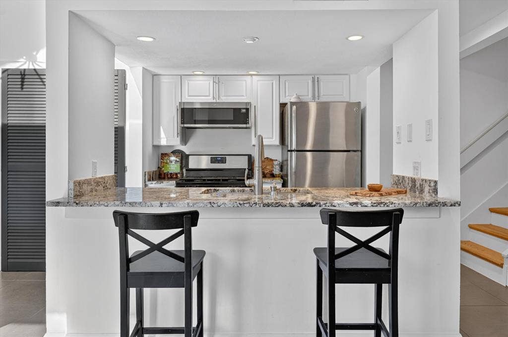 Kitchen featuring stainless steel appliances, white cabinetry, a bar-height counter with a stone surface, and recessed lighting