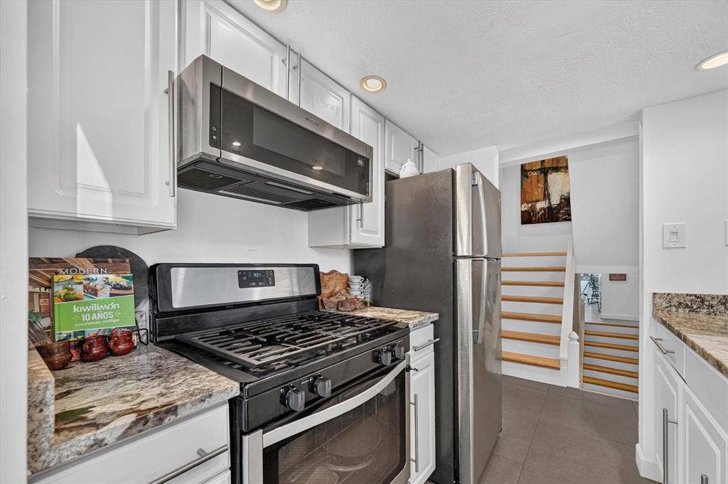 Stainless steel appliances, white cabinetry, recessed lighting, stone countertops, and a built-in microwave