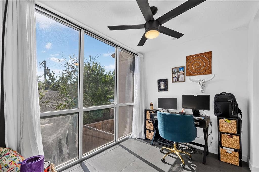 Floor-to-ceiling windows, modern black ceiling fan with integrated lighting, hard surface flooring, white walls, and built-in window coverings