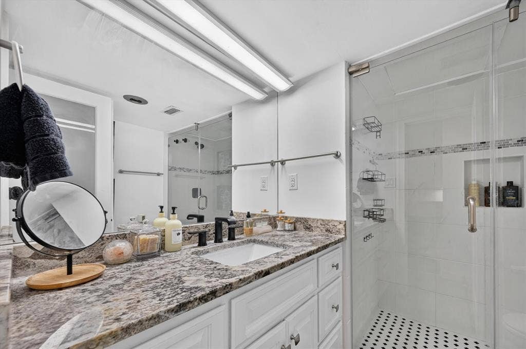 White vanity with integrated sink, granite-style countertop, matte black faucet, and glass-enclosed shower with mosaic tile accent