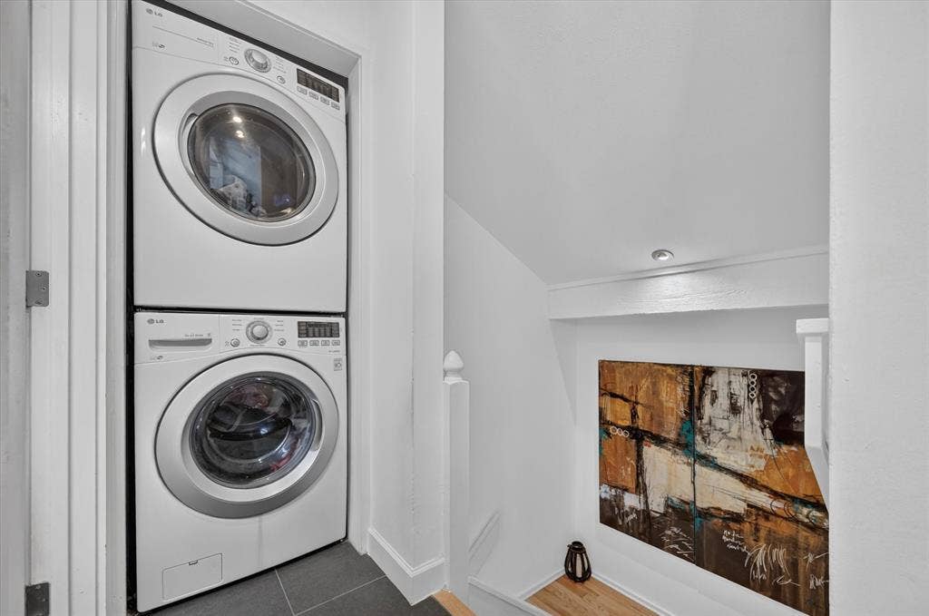 Stacked laundry appliances, recessed ceiling lighting, and dark tile flooring