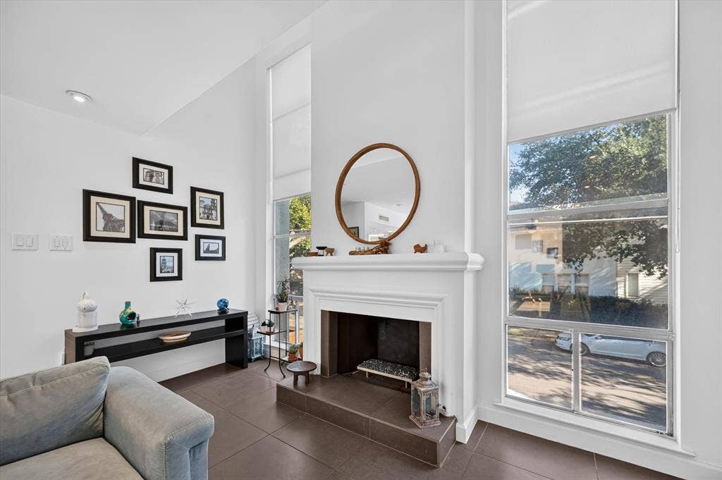 Fireplace with a classic white mantel, large windows with roller shades, recessed lighting, and dark tile flooring
