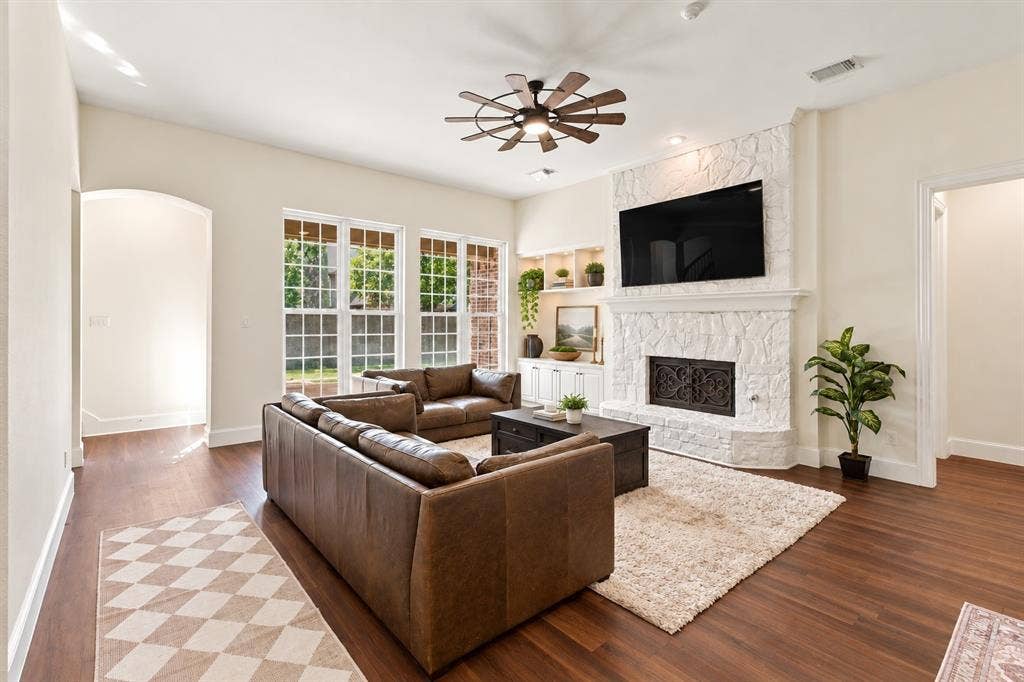 Spacious living area featuring wood-finish flooring, a stone-clad fireplace with mantel, recessed ceiling lighting, and a ceiling fan