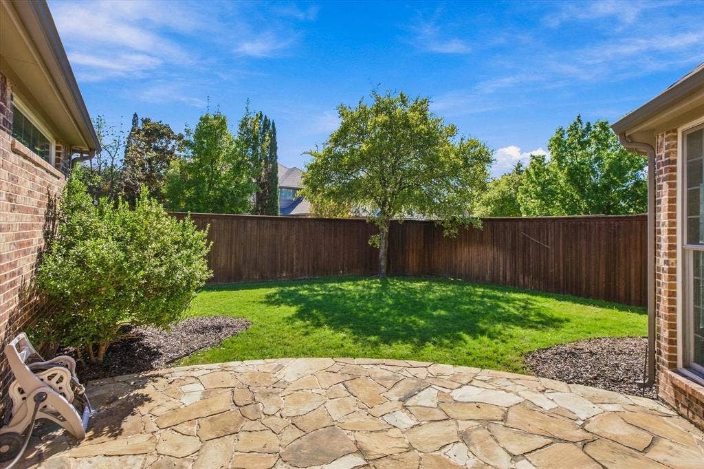 Expansive backyard featuring a natural stone patio, manicured lawn, and privacy fencing
