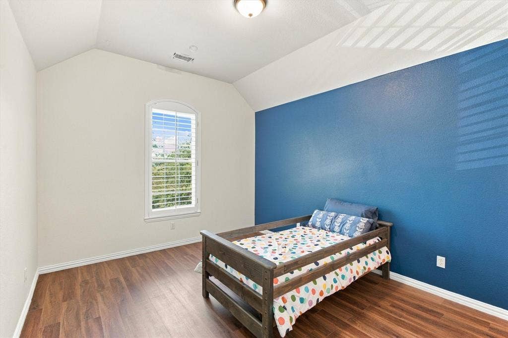 Vaulted ceiling, arched window with plantation shutters, wood-finish flooring, and a flush mount ceiling light