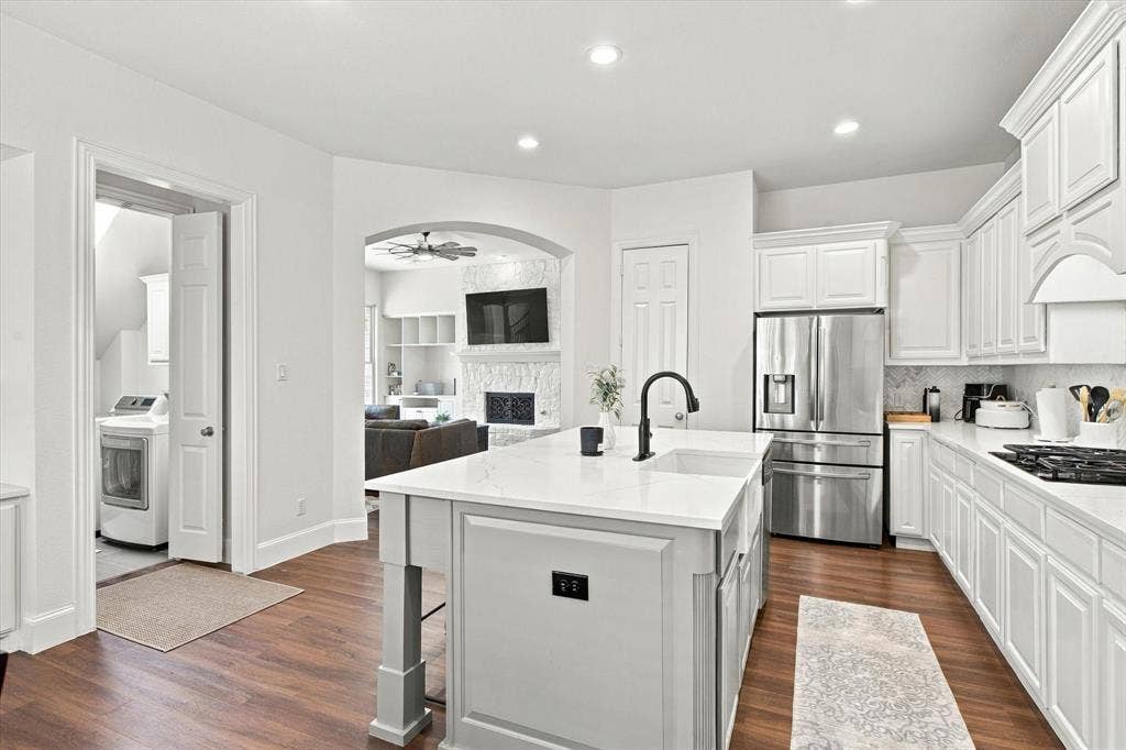 Kitchen featuring an island with a white countertop and undermount sink, stainless steel appliances, white cabinetry, and wood-finish flooring