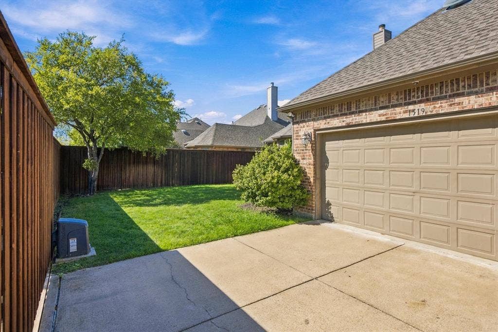 Brick exterior with a two-car garage, concrete driveway, and a fenced backyard with a lawn
