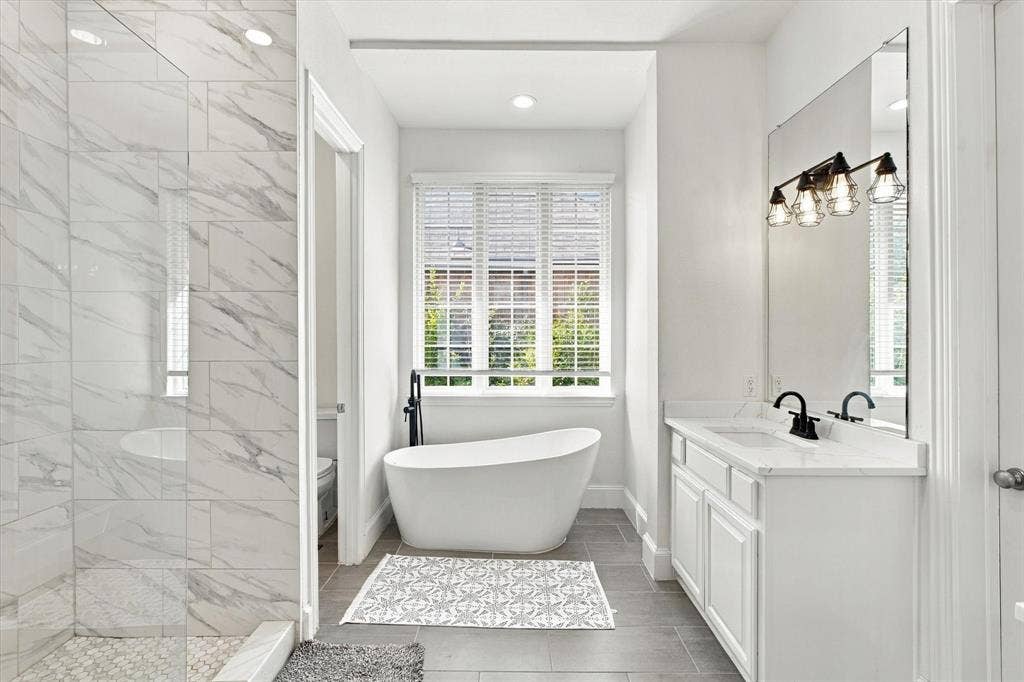 Freestanding soaking tub, dual vanity with undermount sinks, full-height mirror, and a tiled shower with glass enclosure