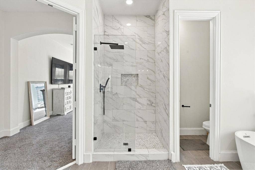 Glass-enclosed shower with full-height marble-style tile surround and recessed shelving