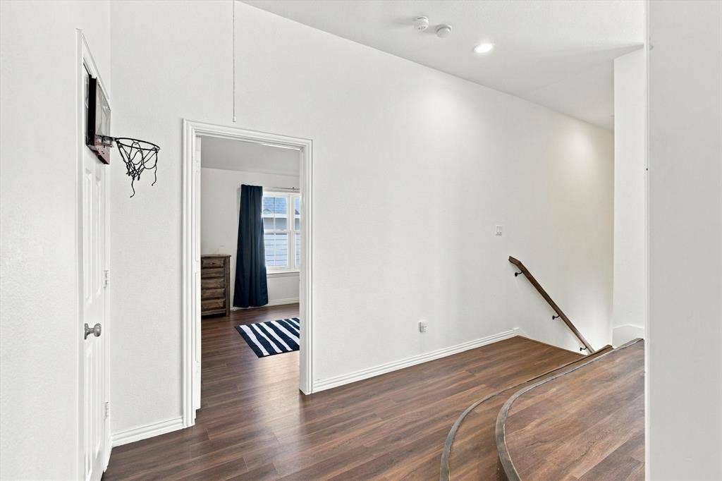 Wood-finish flooring throughout, white painted walls, recessed lighting, and a wood handrail