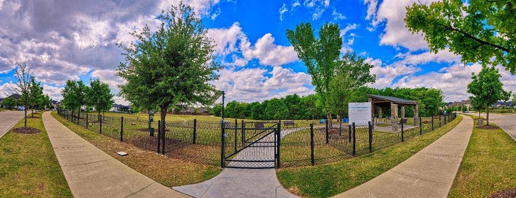 Fenced recreational area featuring a covered pavilion, paved walking paths, and mature trees