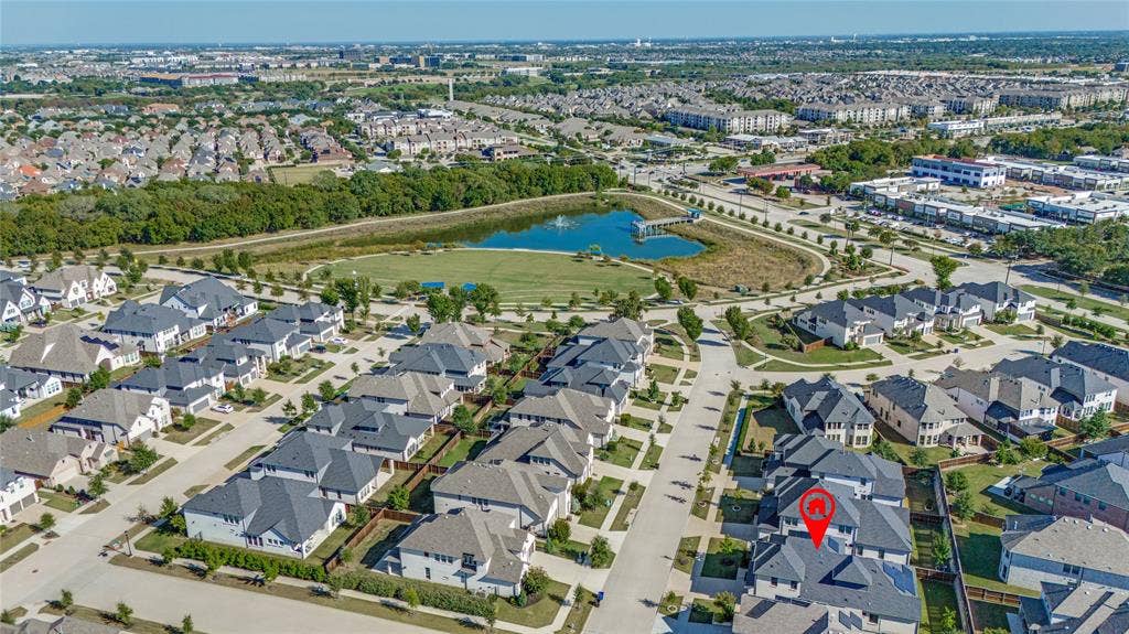 Aerial perspective of a suburban community featuring a prominent pond, surrounding green space, and residential properties with dark-pitched roofs