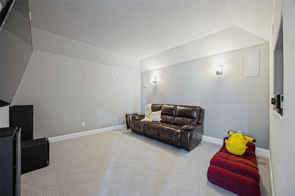 Sloped ceiling with recessed lighting, wall-mounted light fixtures, textured carpet flooring, and integrated wall speakers