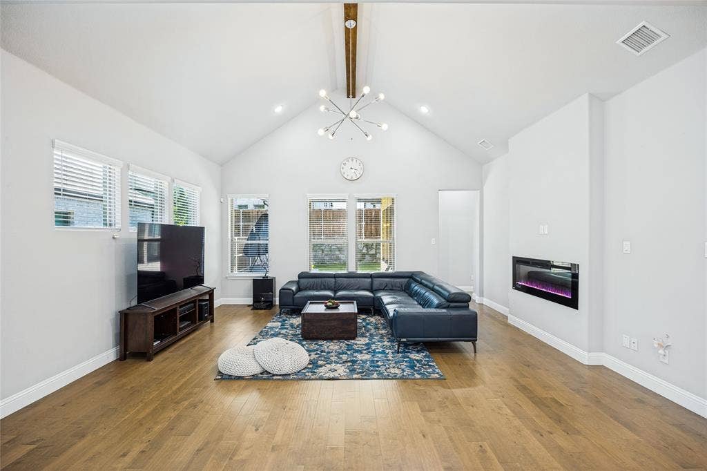 Vaulted ceilings, wood-finish flooring, multiple windows, built-in electric fireplace, and a modern chandelier