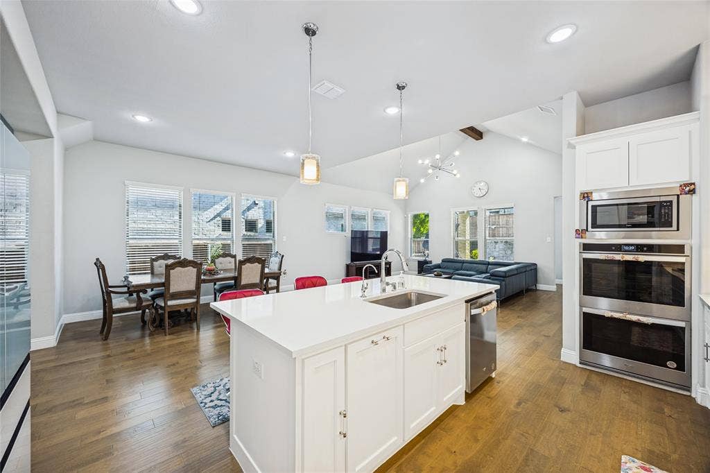 Kitchen island with integrated sink, stainless steel appliances, wood-finish flooring, vaulted ceiling, and recessed lighting