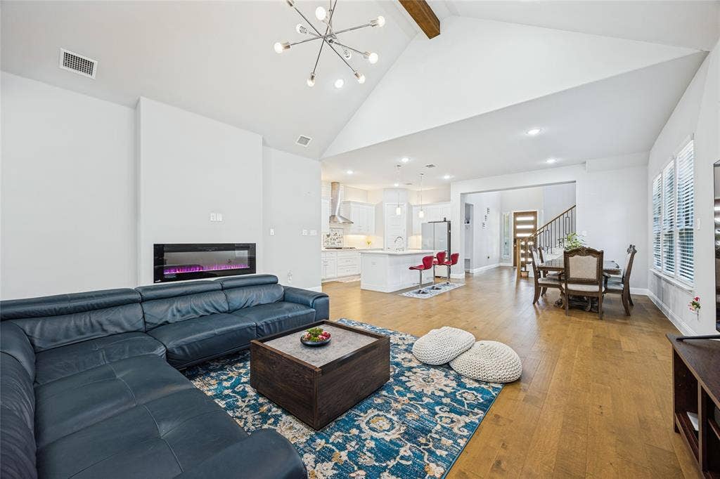 Vaulted ceilings with an exposed wood beam, contemporary chandelier, wood-finish flooring, and a modern linear fireplace