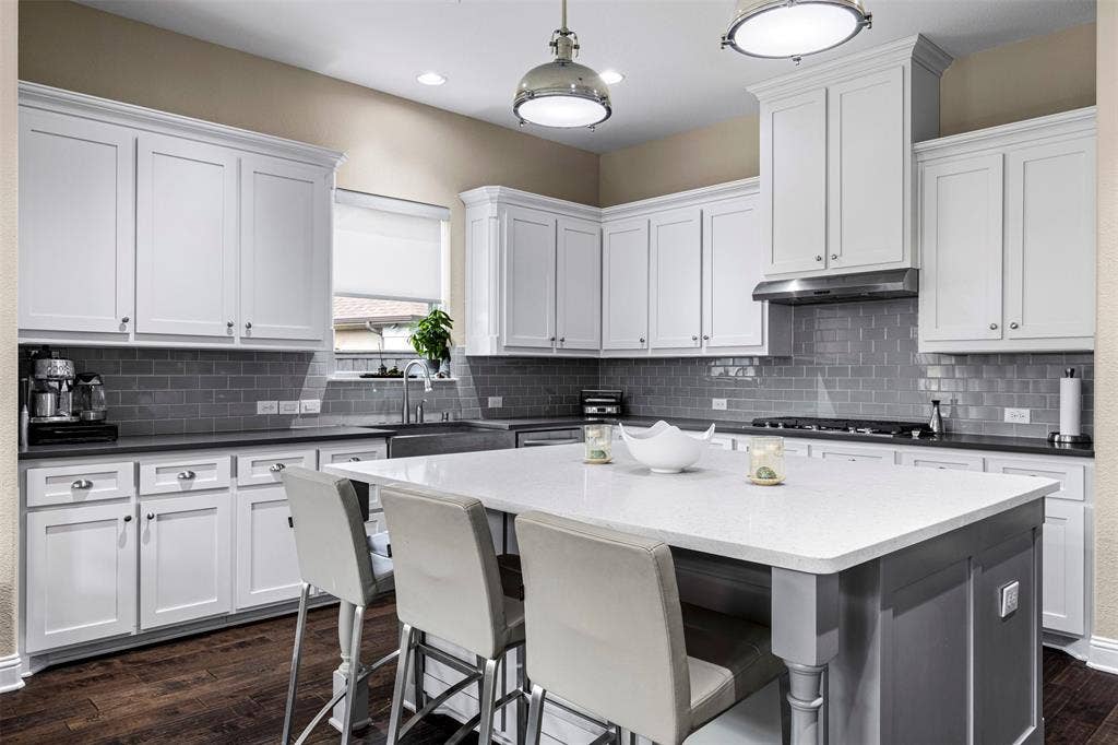 Kitchen featuring white cabinetry, center island with stone-finish countertop, stainless steel range hood, subway tile backsplash, and wood-finish flooring