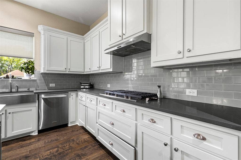 Kitchen featuring white shaker-style cabinetry, dark stone countertops, stainless steel appliances, subway tile backsplash, and wood-finish flooring