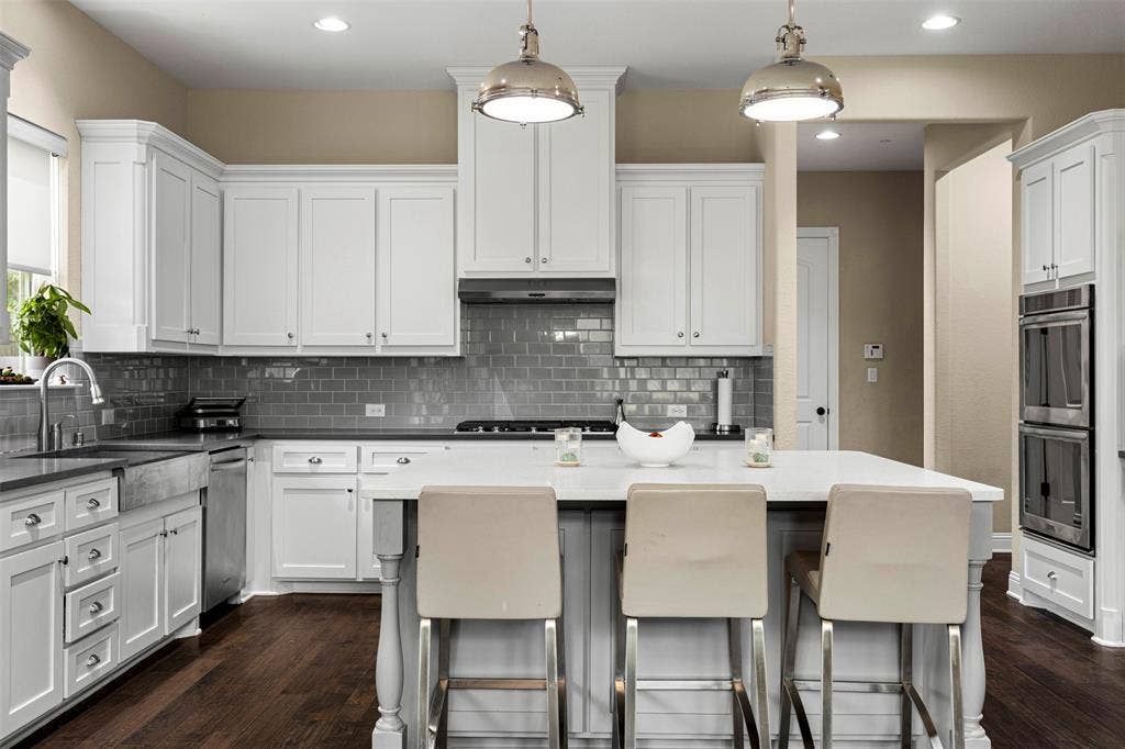 Kitchen featuring white cabinetry, center island with stone countertop, subway tile backsplash, stainless steel farmhouse sink, and built-in double wall oven