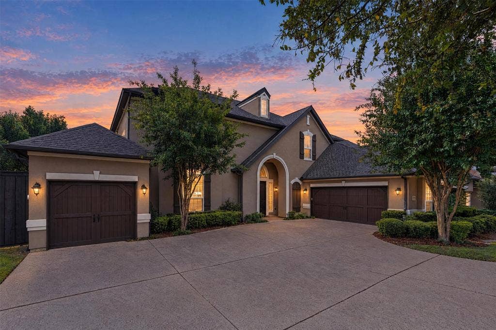 Multi-gabled exterior featuring stucco facade, arched entryway, and dark-toned multi-car garages with carriage-style detailing