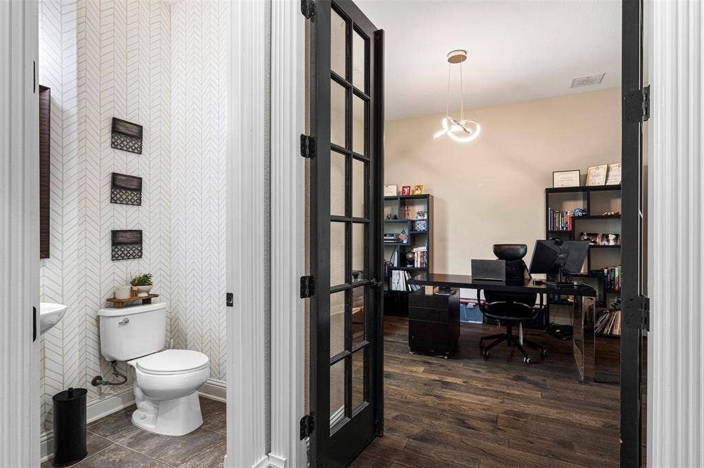 Powder room featuring patterned wallcovering and wood-finish flooring, highlighted by black-framed French doors and modern pendant lighting