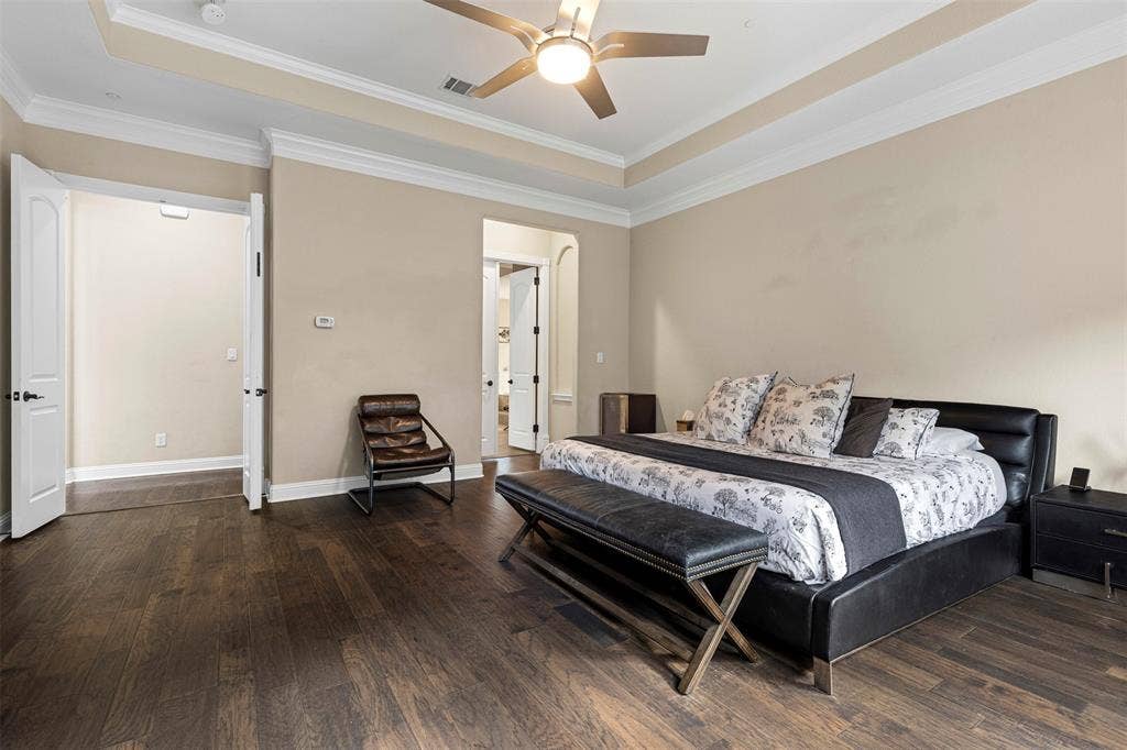 Room featuring dark wood-finish flooring, tray ceiling with crown molding, and a central ceiling fan with integrated lighting