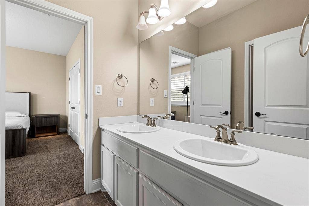 Dual-vanity bathroom featuring white cabinetry, a solid-surface countertop with integrated basins, brushed nickel hardware, and a full-width wall mirror