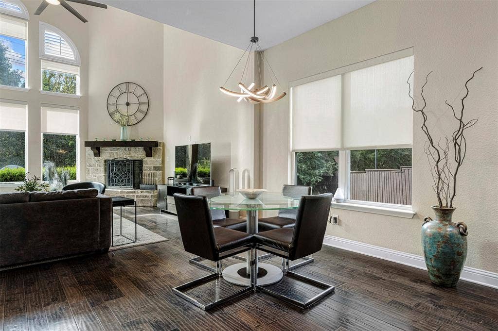High-ceilinged living area featuring wood-finish flooring, a floor-to-ceiling stone-faced fireplace with a timber mantel, expansive arched windows, and a modern sculptural chandelier