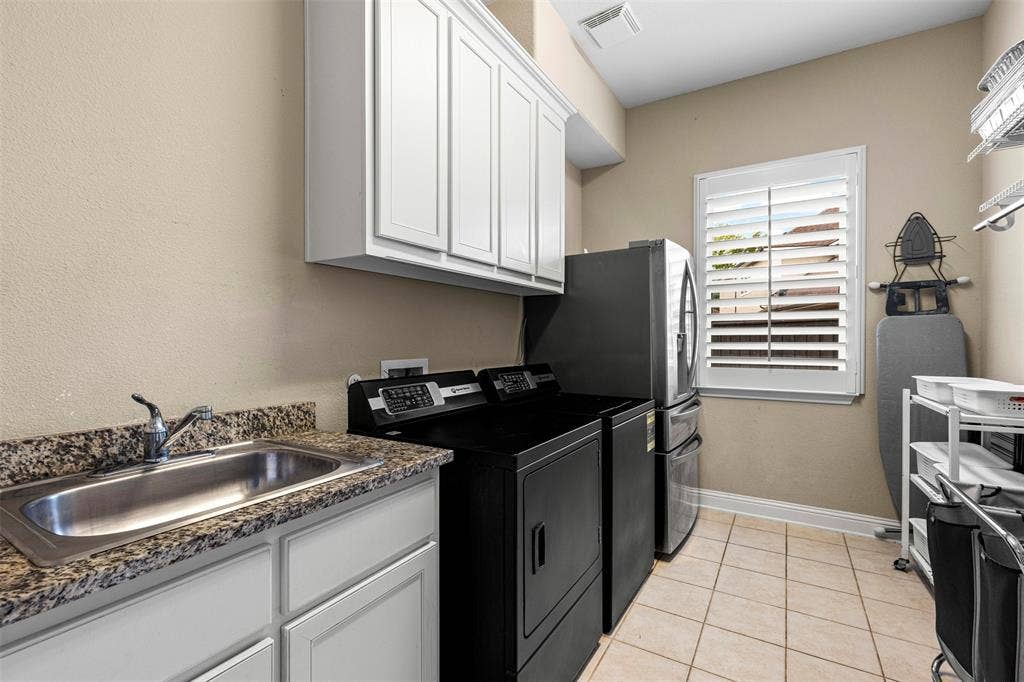Utility room featuring white cabinetry, stone-finish countertops, stainless steel drop-in sink, tile flooring, and louvered window shutters