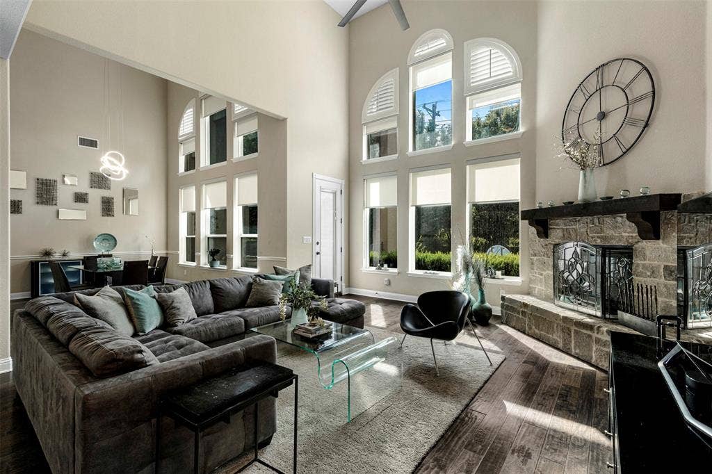 Two-story vaulted ceiling with expansive arched windows, stone-surround fireplace with a dark timber mantel, and wood-finish flooring
