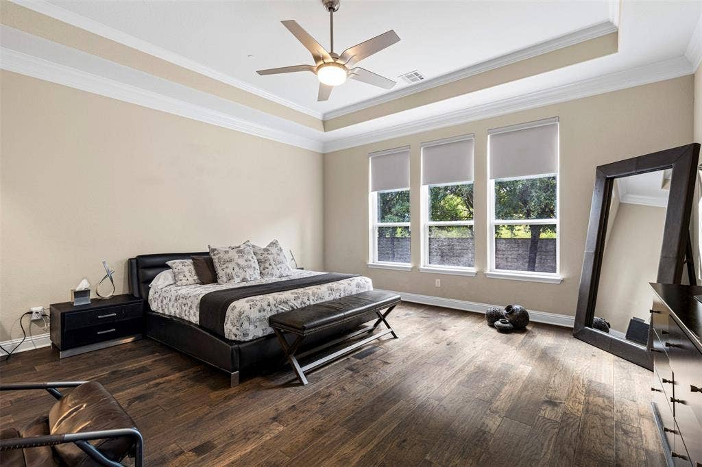 Tray ceiling with crown molding, wood-finish flooring, and a multi-blade ceiling fan with integrated light fixture