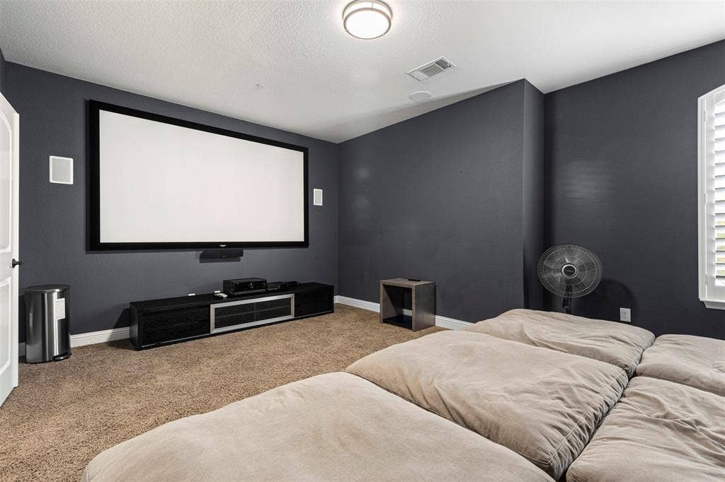 Media room featuring wall-mounted projection screen, integrated wall speakers, recessed ceiling lighting, and plantation shutters