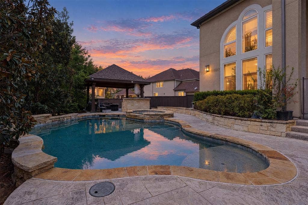 Custom-designed swimming pool with integrated spa and stone coping, accompanied by a covered pavilion featuring a built-in stone outdoor kitchen