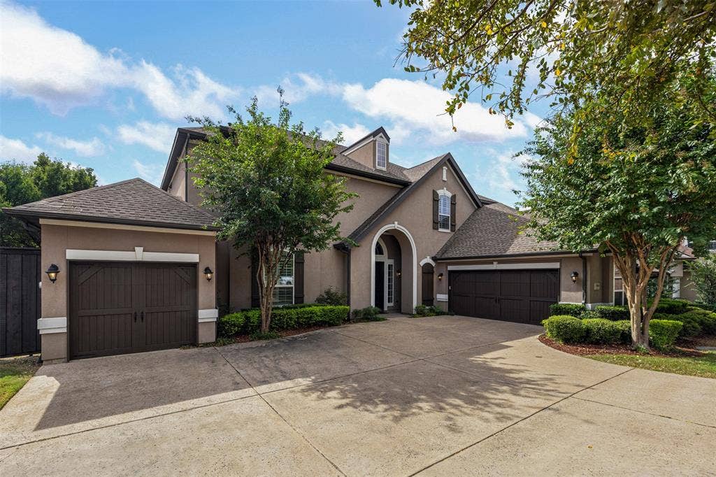 Stucco exterior featuring a multi-gabled roofline, an arched entryway, two separate garage bays with carriage-style doors, and mature landscaping