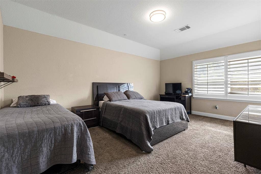 Room featuring high ceilings, wall-to-wall carpeting, and windows fitted with white plantation shutters