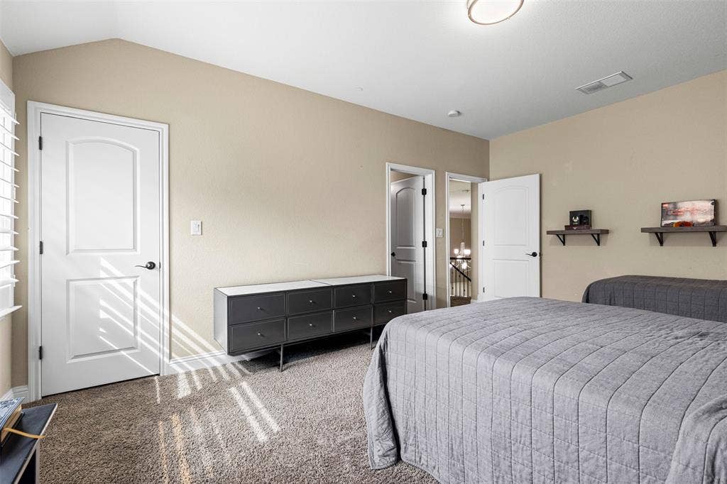 Vaulted ceilings, neutral wall tones, carpeted flooring, two interior panel doors, and wall-mounted floating shelves