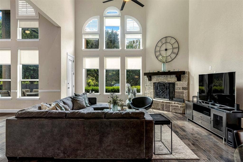 Living area featuring vaulted ceilings, floor-to-ceiling windows with arched transoms, stone-faced fireplace with a wood mantel, and wood-finish flooring