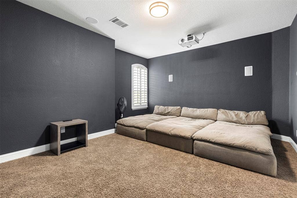 Room featuring wall-to-wall carpeting, ceiling-mounted projector, built-in wall speakers, and an arched window with plantation shutters