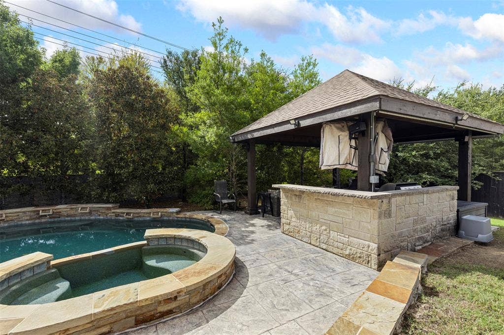 Outdoor living area featuring a covered stone bar, in-ground pool with a raised stone spa, and stamped concrete patio flooring