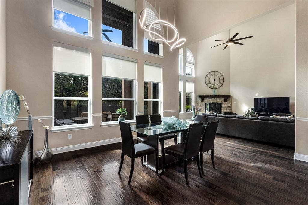 Vaulted ceilings featuring floor-to-ceiling multi-pane windows, wood-finish flooring, a stone-surround fireplace with a wooden mantel, and a contemporary architectural light fixture