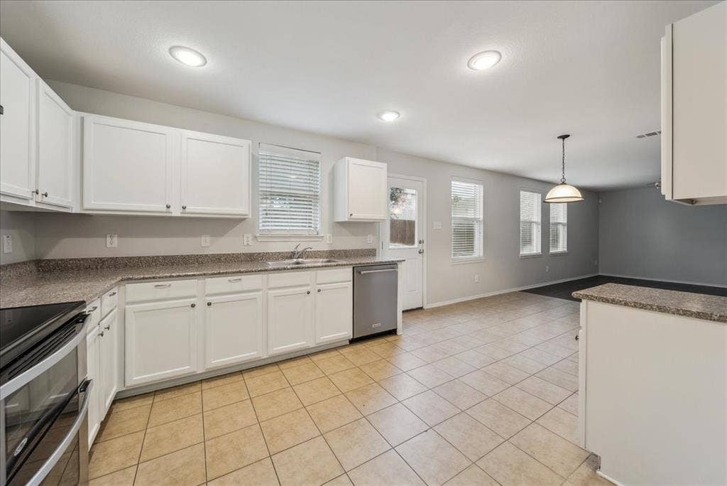 Kitchen featuring white cabinetry, stone-look countertops, stainless steel appliances, and tile flooring