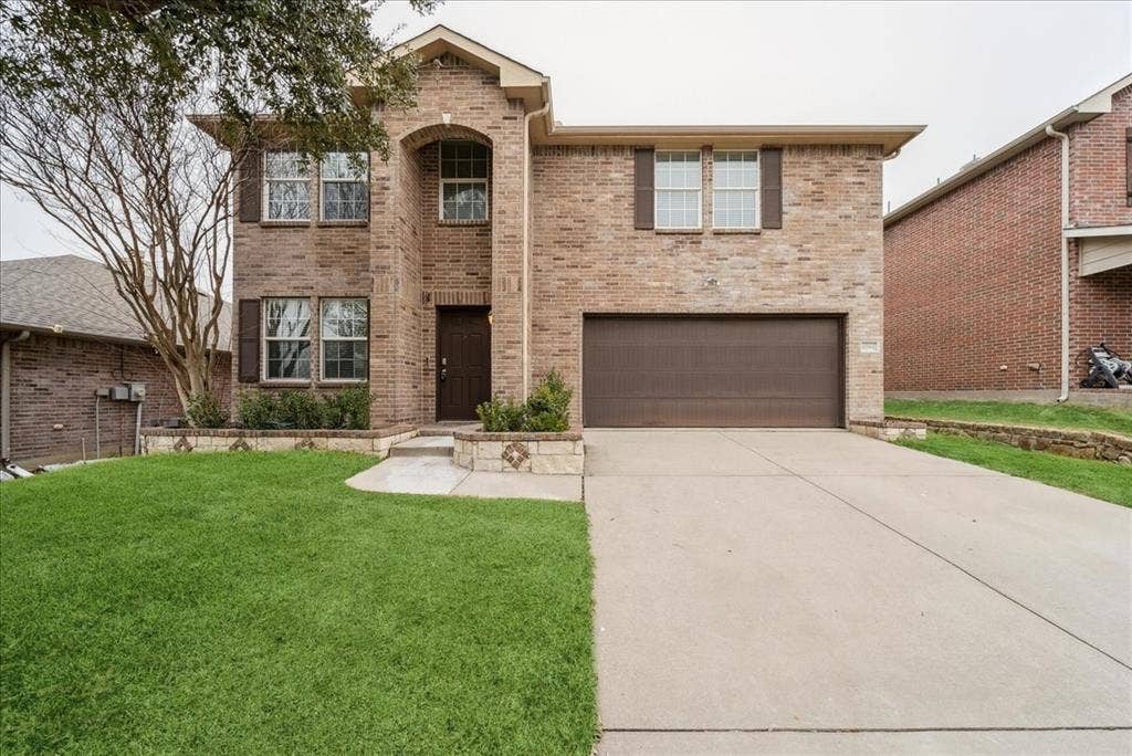 Brick exterior with stone accents, arched entry, two-car garage, and established front landscaping