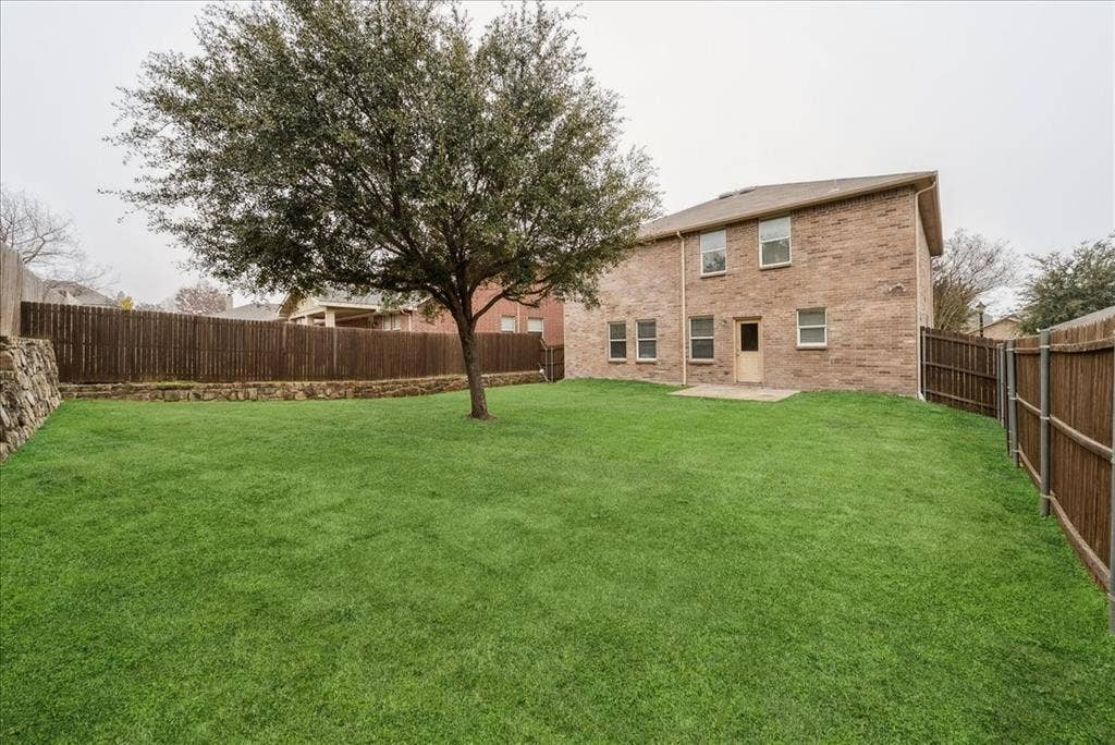 Expansive green lawn with a mature tree, stone retaining wall, and wood privacy fencing