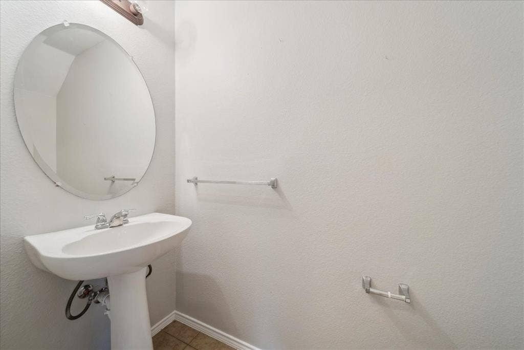 Pedestal sink with chrome faucet, oval mirror, and tile flooring