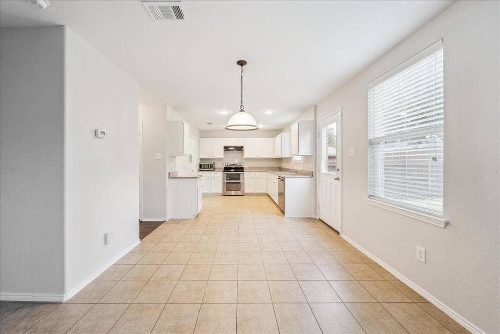 Spacious open-concept area featuring tile flooring, a kitchen with white cabinetry, stainless steel appliances, and ample counter space