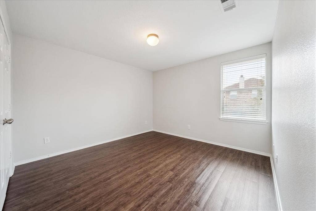 Spacious room featuring wood-finish flooring, neutral-toned walls, and a window with blinds