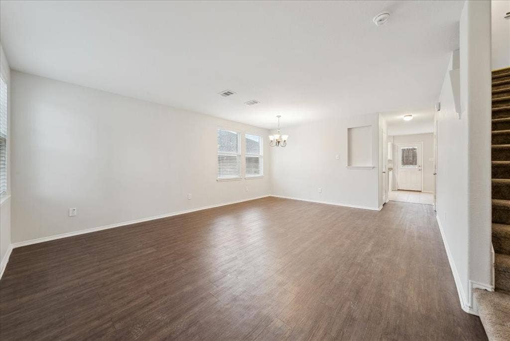 Expansive open-concept living area with wood-finish flooring, multiple windows, and a chandelier
